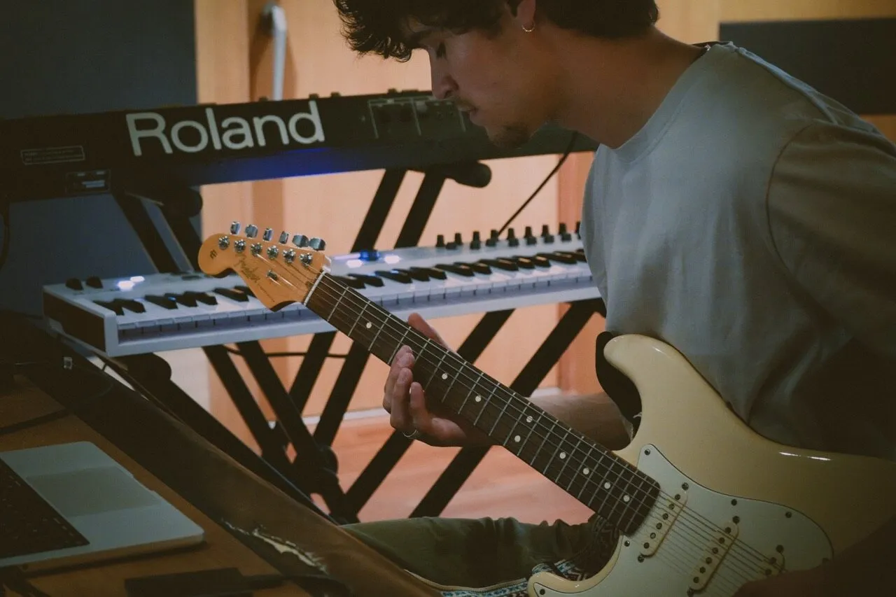 A musician playing an electric guitar next to a Roland keyboard